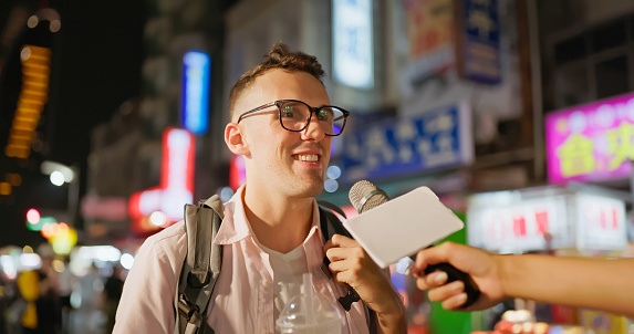 aucasian man is interviewed while he visiting the night market in the evening