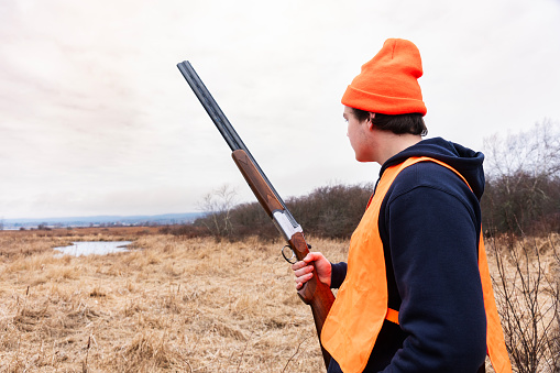 A young male hunter holding shotgun while out bird hunting in the winter