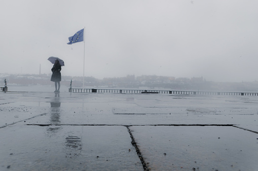 Unrecognizable person standing with a umbrella at a flag pole