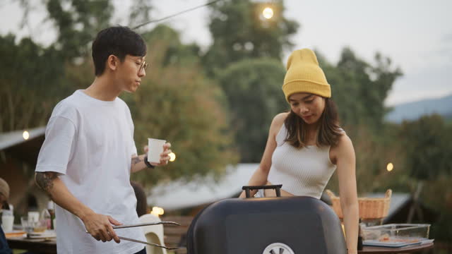 Asian man helping woman with barbecue dinner on mountain