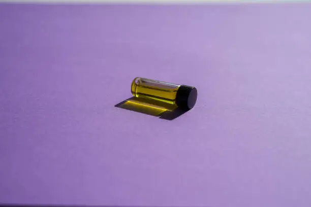 Small bottle of essential oil laying on its side on a bright purple background with light shining through it