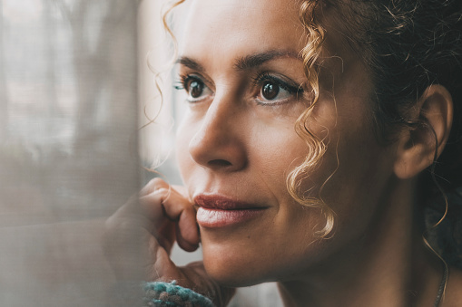 One confident lady contemplate outside the window at home with dreaming and thoughtful expression on face. Portrait of adult female people in indoor thinking leisure activity alone with window light