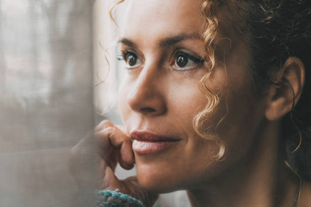 One confident lady contemplate outside the window at home with dreaming and thoughtful expression on face. Portrait of adult female people in indoor thinking leisure activity alone with window light stock photo