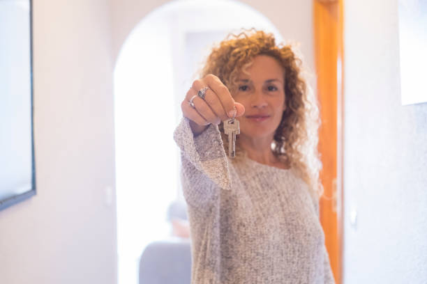 une femme debout à la maison montrant à la caméra une nouvelle clé. maison, acheter des biens immobiliers, louer, propriété, concept, personnes. nouvelle vie de femme avec porte-clés à portée de main. image de prêt hypothécaire avec dame - adventure business horizontal real estate photos et images de collection