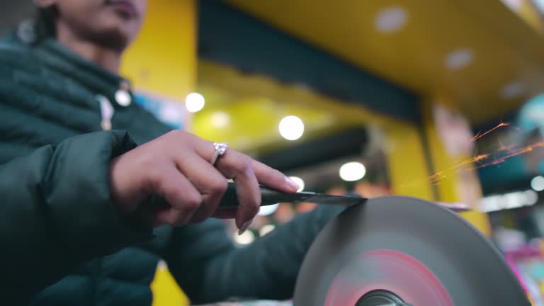 Woman sharpens knfe using a grinder machine.