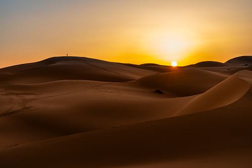 Silhouette of man standing on a distant sand dune at sunset in the Sahara Desert, Morocco