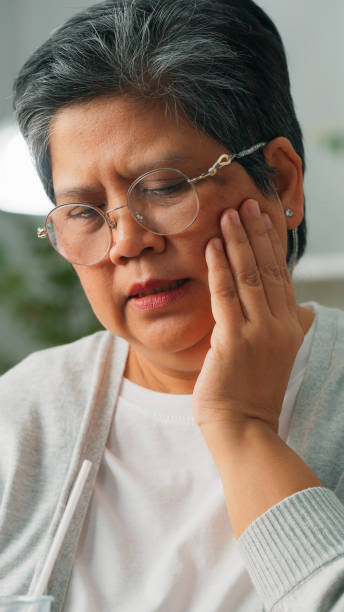 istock Unhealthy senior Asian woman with teeth problem touching cheek while sitting on couch at home, Unhappy grandmother suffering from sensitive teeth, Elderly woman having teeth pain 1897778537