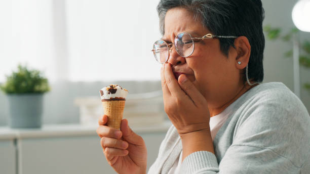 istock Elderly Asian grandmother suffering from sensitive teeth while eating ice cream and sitting on couch at home, Senior woman suffering from dental problem, Lady with sore mouth 1897780086