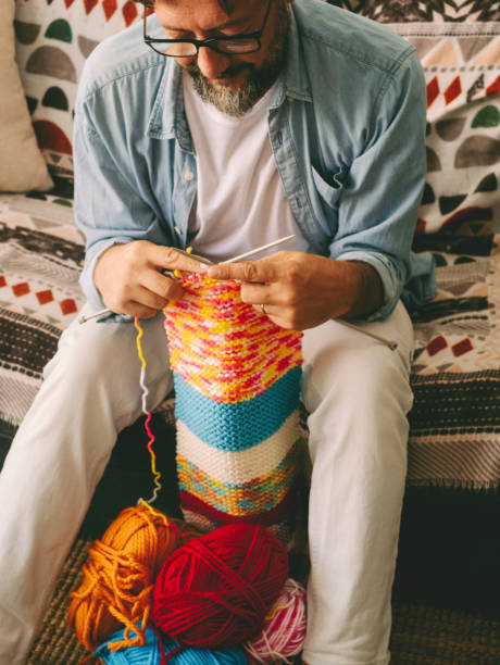 istock One man at home busy in new hobby activity doing knitting work with wool and needles. Single male mature in indoor leisure activity alone. People in alternative work. Sitting on sofa in apartment 1897954165