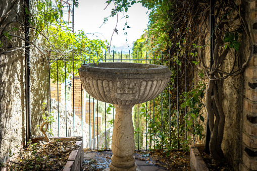 Urban garden with a square high pond built from natural rock with a small waterfall created by a stainless steel outlet which is mounted on a vertical wooden beam, surrounded by green grass