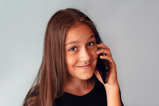 Happy joyful charming caucasian kid girl wearing black dress on blue background talk speak phone smile good mood