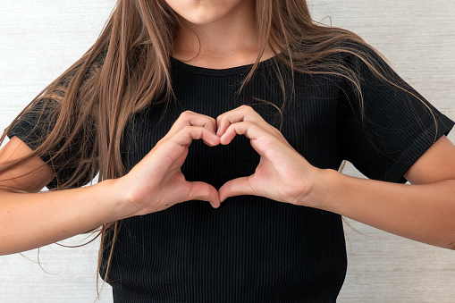 female hands forming a heart shape. A teenage girl shows her heart with her hands.