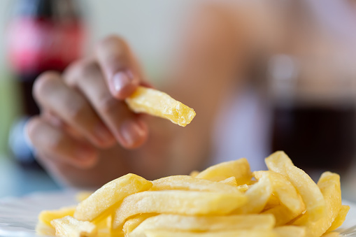 A hand holds French fries in close-up. Eating junk food in a fast food cafe.