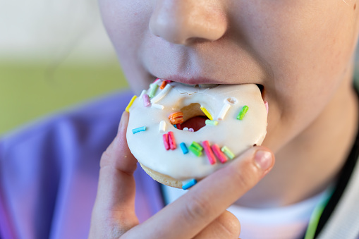 a piece of a chocolate donut in the hand of a teenage girl was bitten off. The concept of an unhealthy breakfast and harm to health from sweets. open mouth and white chocolate donut.