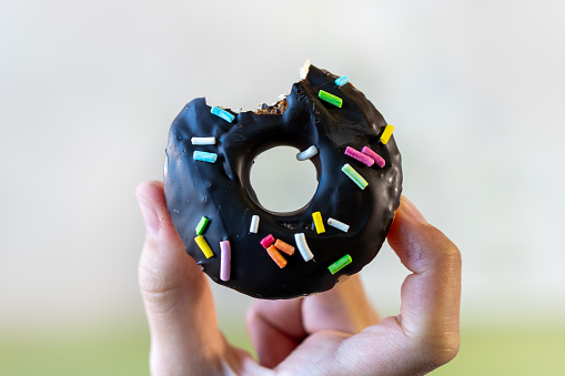 a piece of a chocolate donut in the hand of a teenage girl was bitten off. The concept of an unhealthy breakfast and harm to health from sweets.