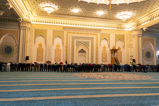 praying Muslims during prayer in a mosque in Tashkent, Uzbekistan. Muslim men during evening prayer inside the mosque.