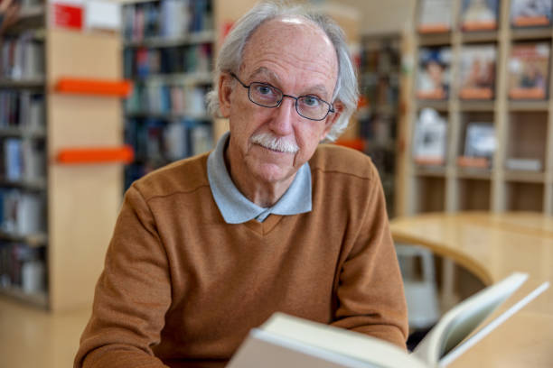 istock Gray-Haired Caucasian Man Looking At Camera While Holding A Book 1898247234