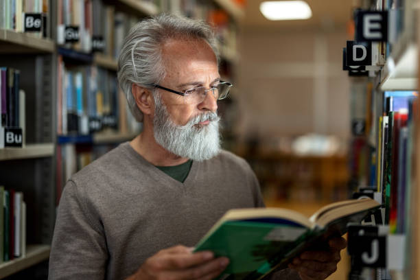 istock Gray-Haired Caucasian Man Reading A Book At The Library 1898248345