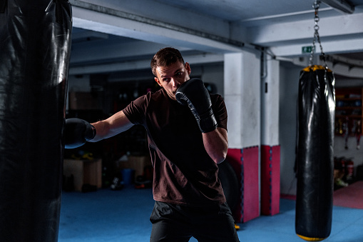 Young Caucasian male kickboxer punching a bag at the gym. He is focused and determined. He is practising punches and kicks.