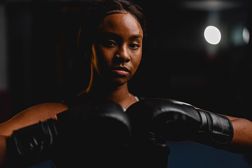 Headshot of a confident young Hispanic female boxer wearing boxing gloves and sports clothes. She is looking at the camera.