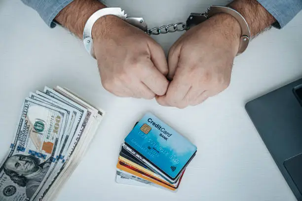 Photo of financial fraud with credit cards concept. Theft of bank accounts.. Person in Handcuffs with a Bank Card on the Table closeup