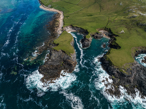 Aerial view of some medium size cliffs located in  Ireland, surrounded with the atlantic ocean waves during a sunny day.
