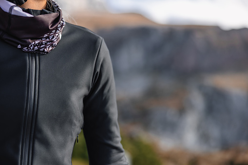 Close-up of the details of cycling gear for women, featuring a close-up shot of a cycling jacket and neck scarf. The mountain reflection in the background adds a sense of adventure to the photo.