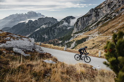 A professional male ride cyclist taking on mountainous terrain. Conquering the challenging natural terrain of the mountain range, wearing full professional gear climbing higher and higher toward the top.