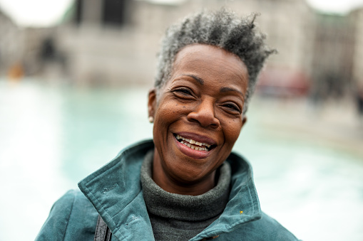 A senior adult black female pensioner laughing at the camera. She has a big smile on her face. The woman has grey hair and is wearing a warm winter jacket. The background is blurred.