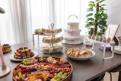 A table at a modern apartment set for a baby shower celebration. The table is decorated with baby shower decorations and is full of various delicious snacks and sweets.