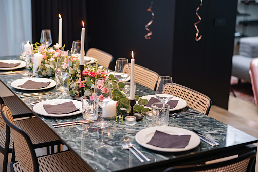 Side view of an amazing dinner table. The blue marble table is decorated with beautiful pink flowers and white candles. The plates are covered with napkins.