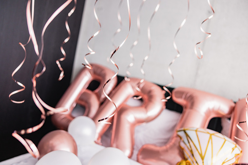 Close-up of beautiful pink balloons on a hotel bed before a bachelorette party. The balloons are spelling the word 'bride'. The room is illuminated by the natural light from the windows. There are strings hanging from the ceiling.