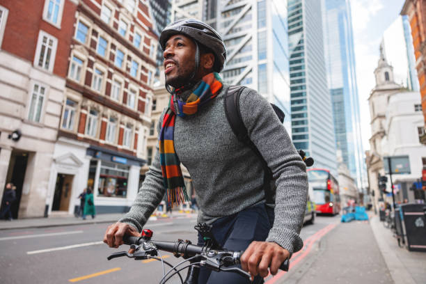maschio adulto nero eco-consapevole che sorride mentre va in bicicletta in città dopo il lavoro - bicycle london england cycling safety foto e immagini stock