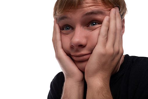 Handsome Caucasian blond teenager guy in a black T-shirt is worried and wants to hide.