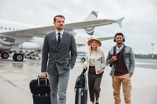 Diverse young adult people walking on the tarmac at the airport. Passengers disembarking the airplane.