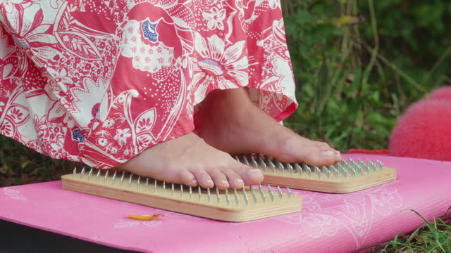 Barefooted feet of woman stands on wooden sadhu yoga board with sharpen nails.