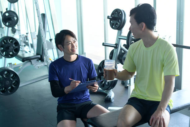 instrutor masculino asiático e membro da academia masculina falando na academia - gym machine smiling coach - fotografias e filmes do acervo