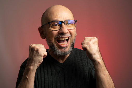 White man, bald, with prescription glasses, smiling and celebrating. Isolated on red background.