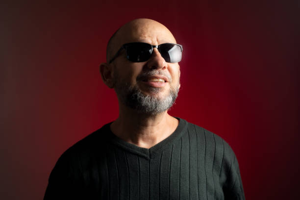 Caucasian, bald man in sunglasses, confident smiling looking up. Isolated on red background.