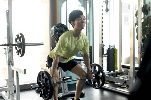 jovem asiático durante musculação levantando barra em ginásio de esportes - gym machine smiling coach - fotografias e filmes do acervo