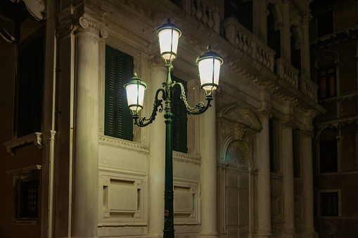 Vintage three lamp street lamp illuminated  in Italian city of Venice at night.