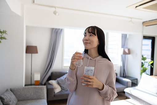Pregnant woman drinking water and taking supplements at home