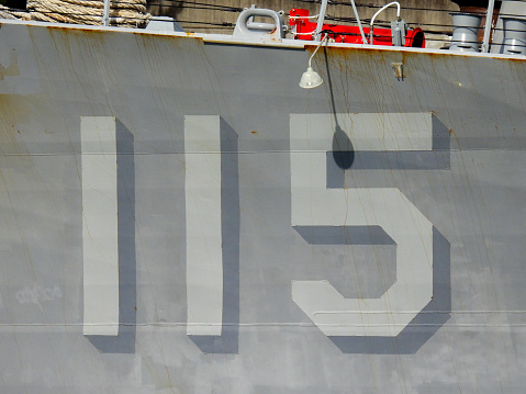 The ship number painted on the hull of USS Rafael Peralta (DDG-115) of the US Navy docked in Garden Island naval base in Sydney Harbour. An electric light which lights her hull at night casts a shadow. This image was taken on a sunny afternoon on 12 August 2023.