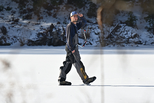 Ice fisherman with auger walking on frozen beaver pond in Washington, Connecticut, winter