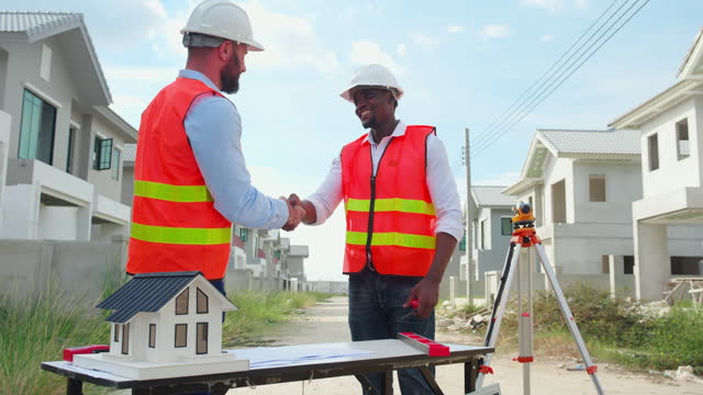 Team young engineer man looking blueprint and handshake for doing agreement together at construction site together, architect talking about project real estate with success for development house.