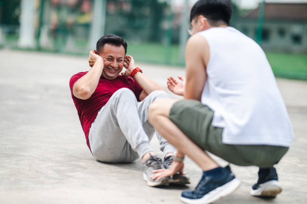 Fitness Drive: Trainer Encouraging Asian Man's Park Sit-Up Workout