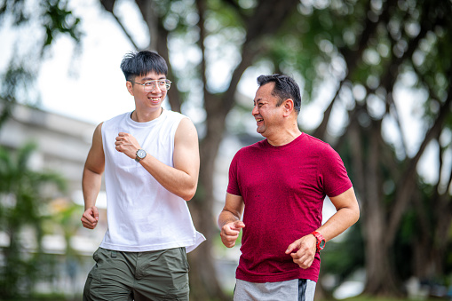 Mature Asian man doing jogging training with his personal young male trainer in the park.