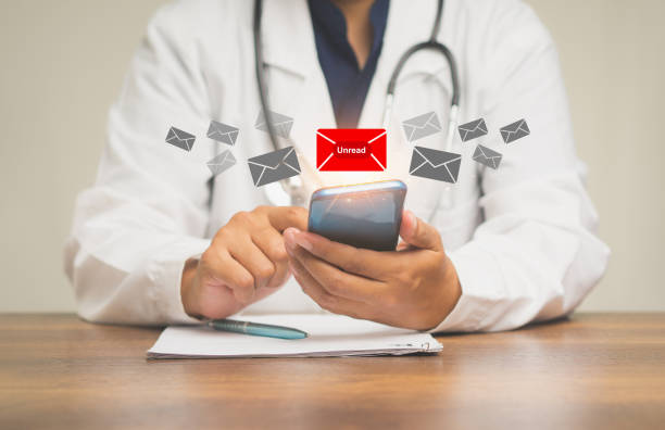 istock Doctor using a mobile receives a new message with unread email icons while sitting at the table. 1898908819
