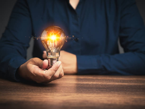 istock Innovative business ideas. Hand of a man holding a lighting bulb with lighting while sitting at the table. 1898917592