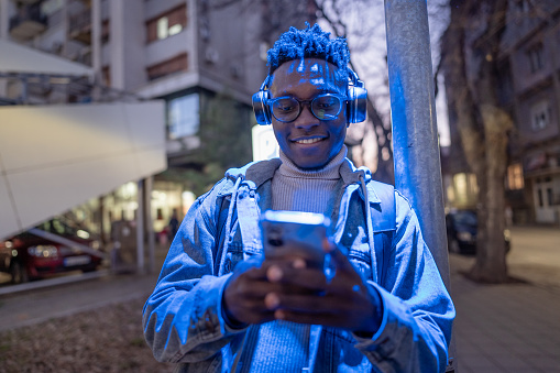 Young man reading a message online on mobile phone while standing in the city in the evening